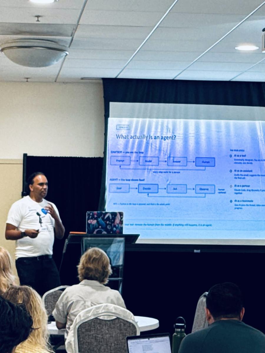 Raj Lal presenting the slide titled What actually is an agent, showing the chatbot loop and the agent loop side by side.
